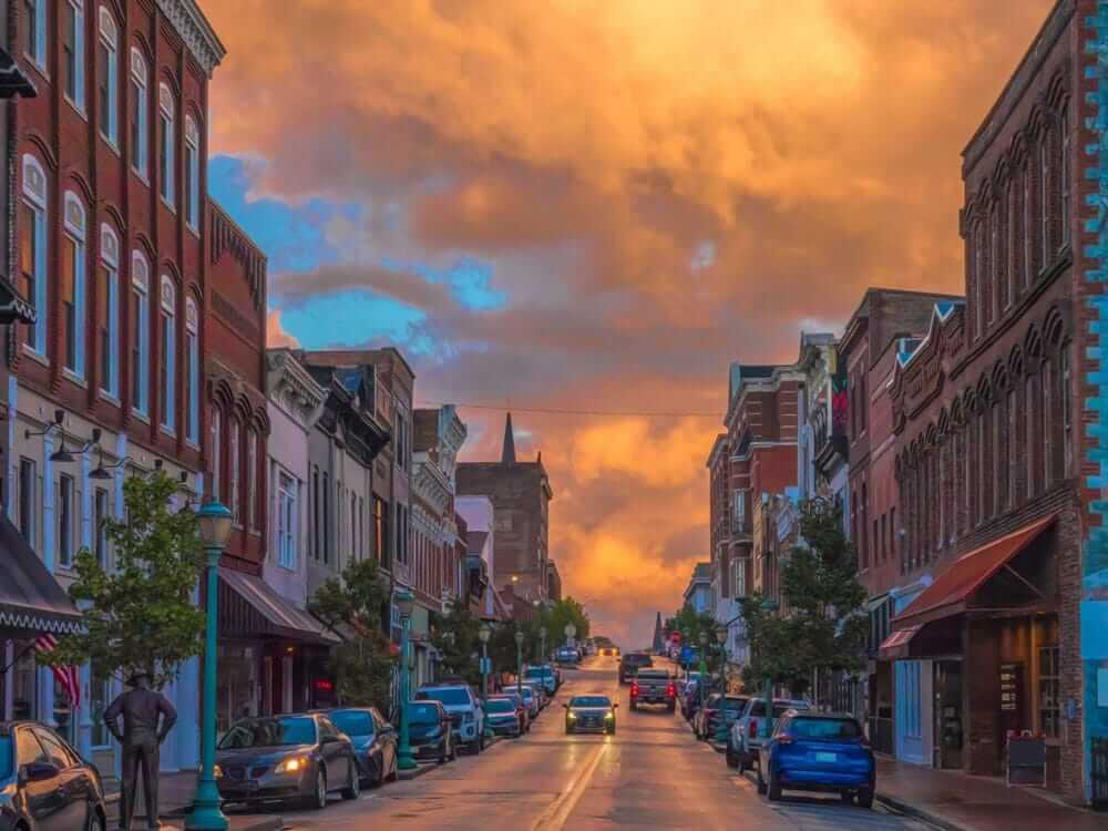 Sunset over historic downtown street lined with cars and brick buildings, capturing vibrant skies.