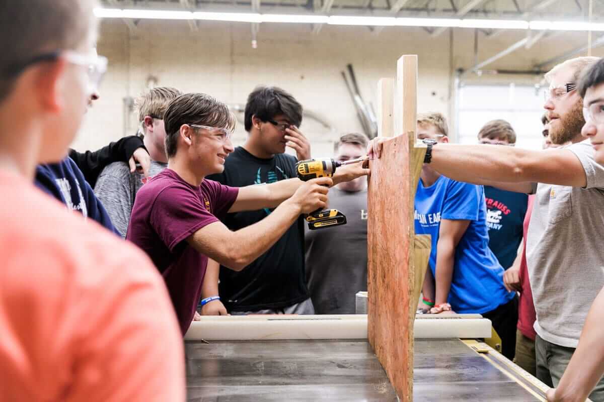 Students learning woodworking with power tools in a classroom workshop.